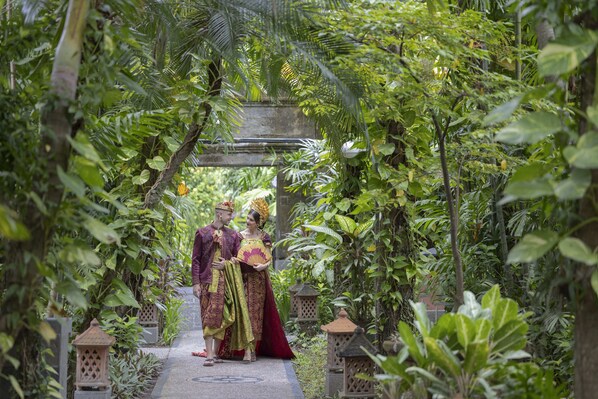 A couple in traditional attire walking through a lush garden pathway. - Tonys Villas & Resort, Seminyak - Bali (Keroboken Kelod)