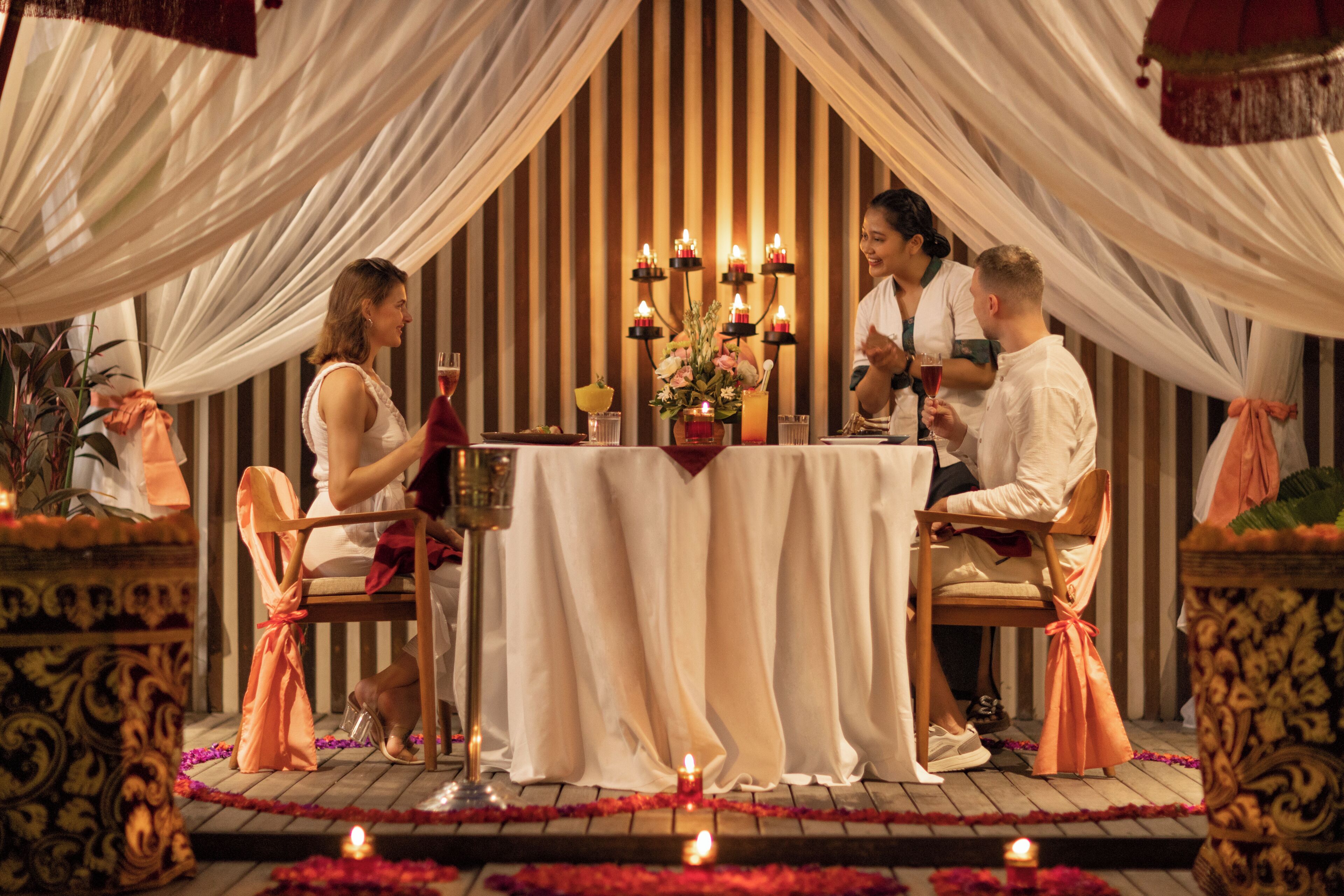 Cena romántica con mesa, sillas, velas y un fondo decorativo.