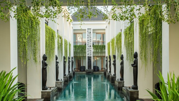 A serene indoor pool area with a central water feature, flanked by statues and lush greenery. - Tonys Villas & Resort (Keroboken Kelod)