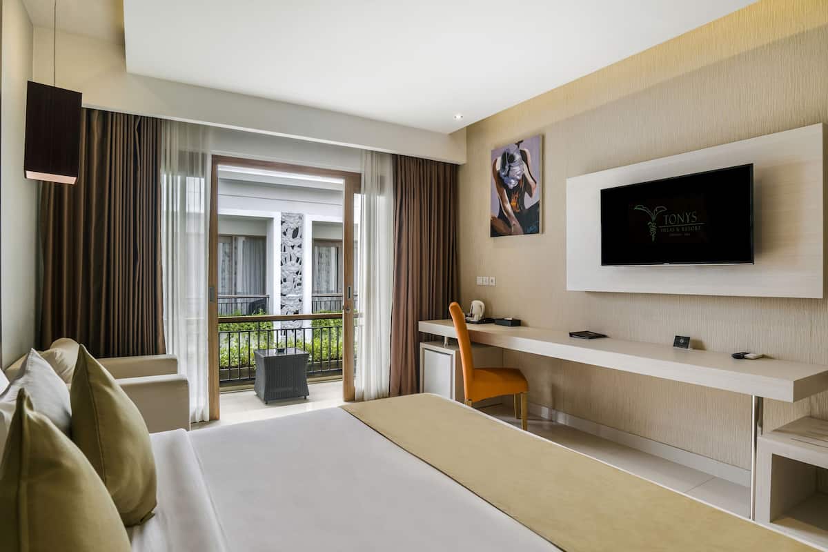 A modern hotel room with a large bed, a desk, a television, and a balcony with curtains.