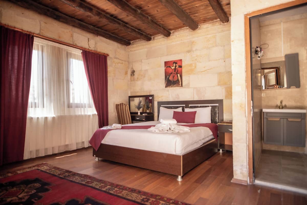 A bedroom with a wooden bed, a nightstand, a mirror, and a stone wall.