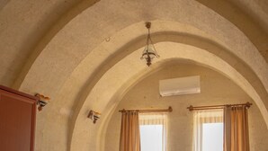 Un dormitorio con una cama grande, dos ventanas con cortinas, un techo abovedado y una lámpara colgante.