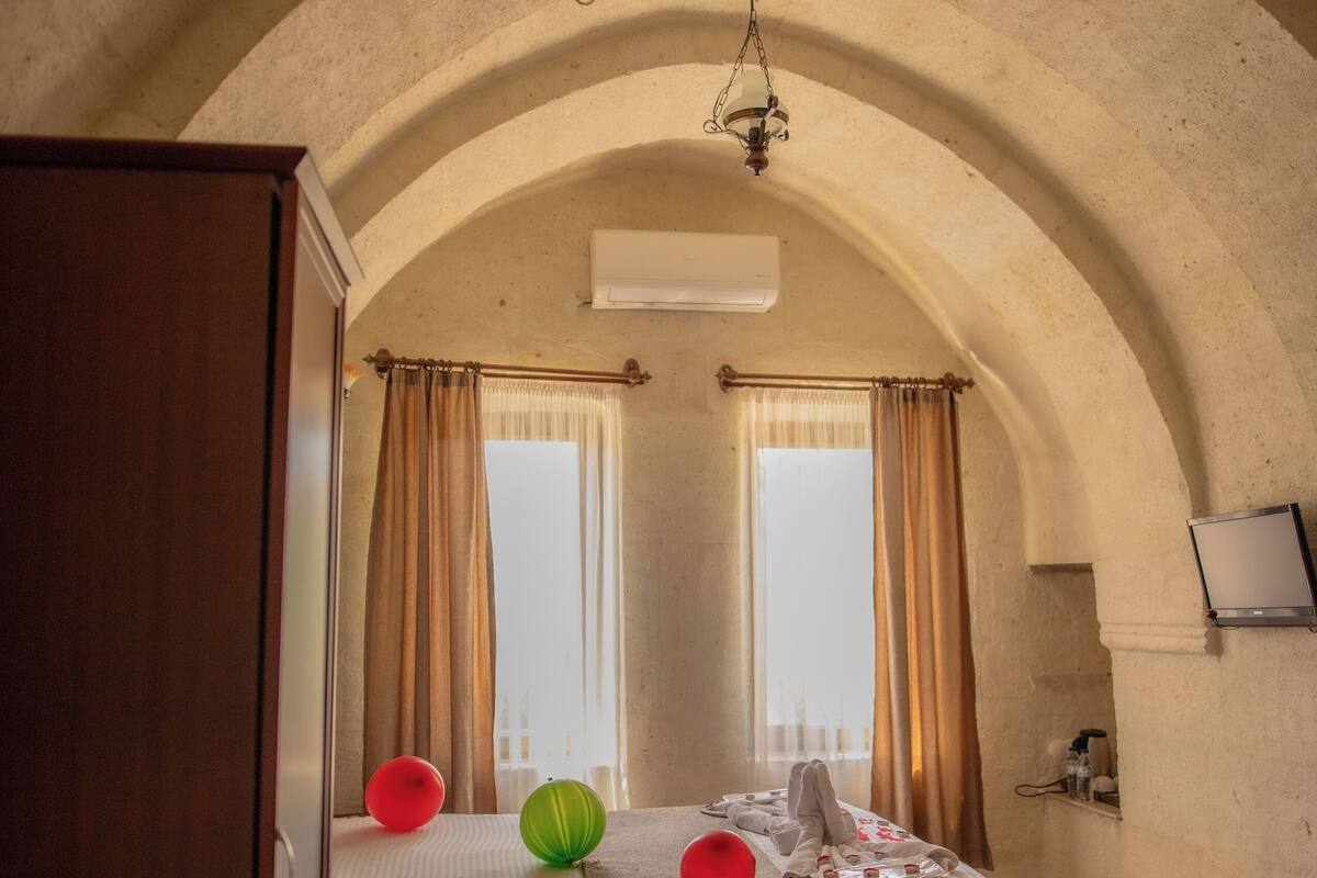 A bedroom with a bed, a wardrobe, a television, and a window with curtains.