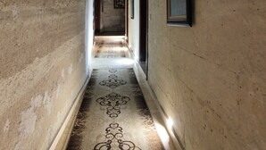 Un pasillo estrecho con alfombra estampada, paredes de piedra y obras de arte enmarcadas.