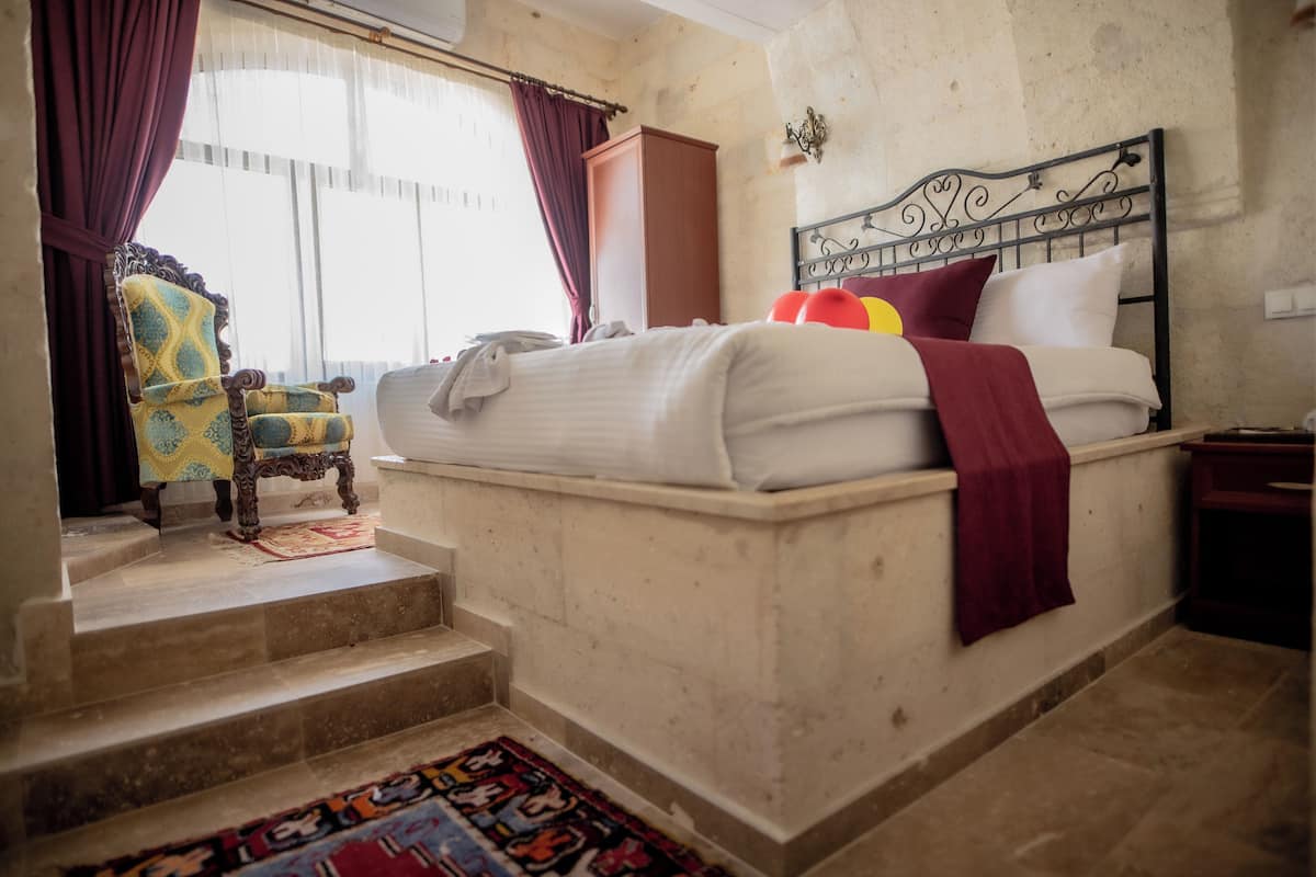 A bedroom with a bed, a chair, a wardrobe, and a window with curtains.