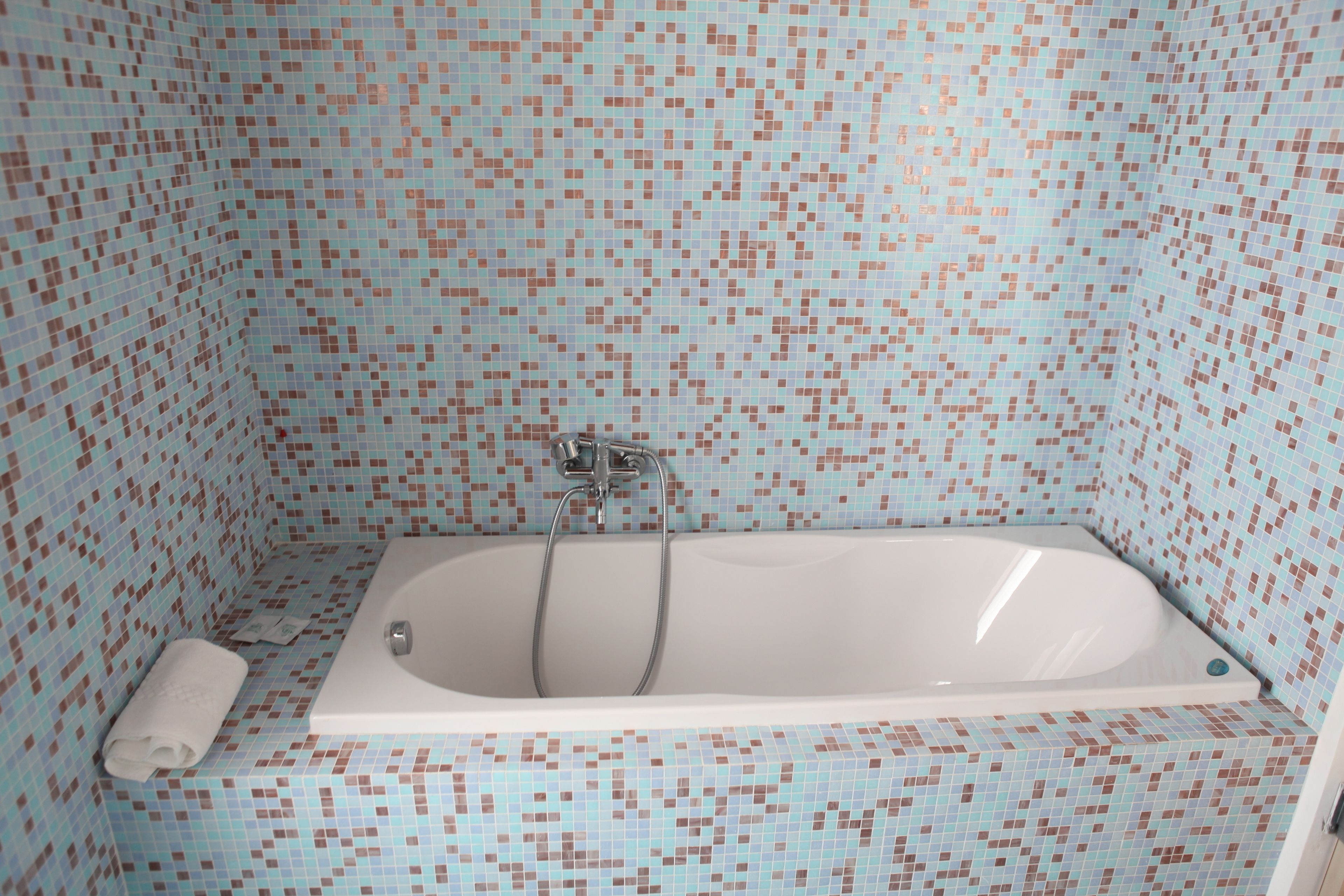 Un bagno con una vasca da bagno bianca, pareti rivestite di piastrelle e un asciugamano sul pavimento.