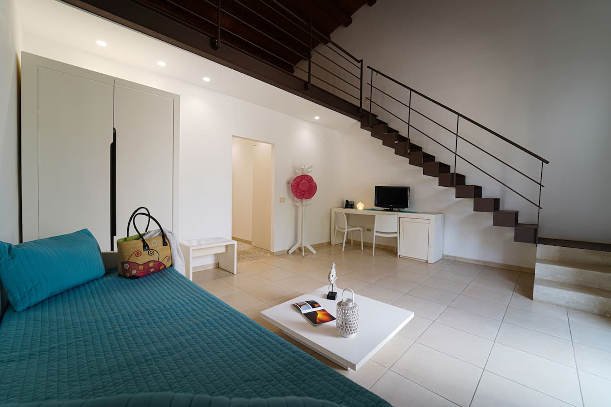 A modern living room with a bed, a desk, and a staircase.