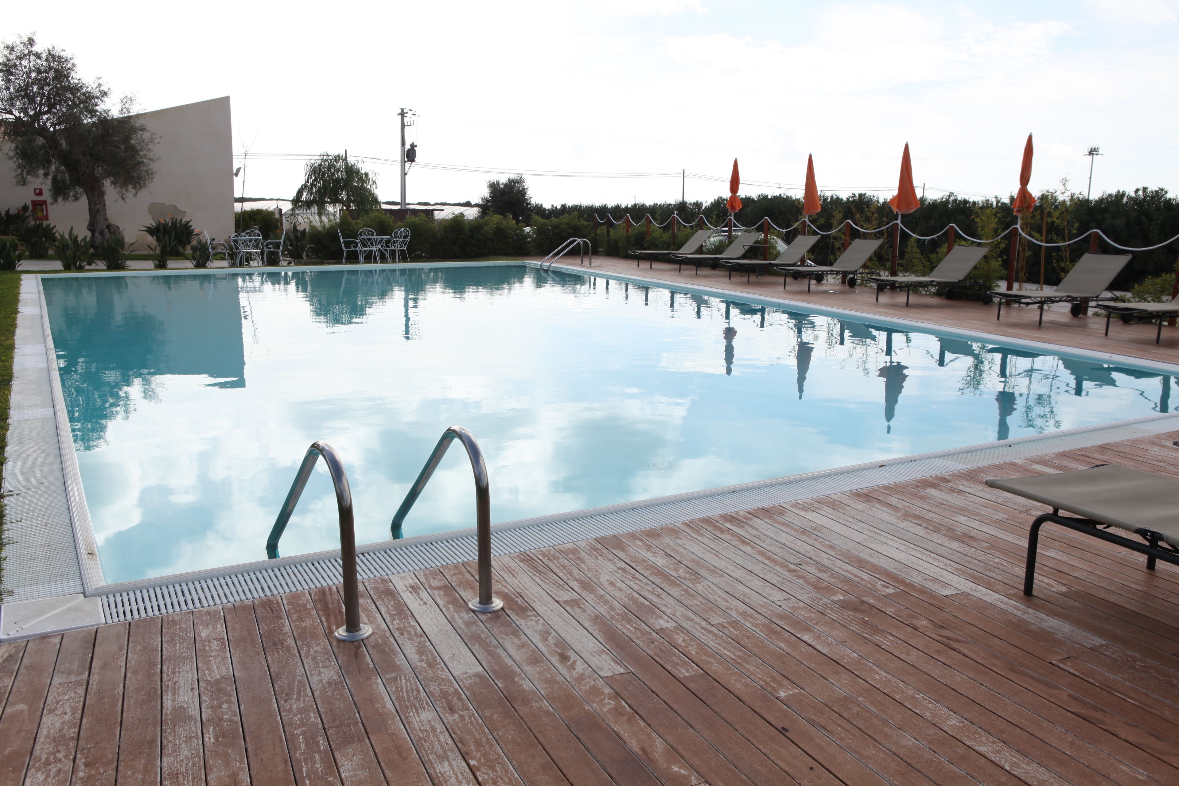 A swimming pool with a wooden deck, lounge chairs, and umbrellas.