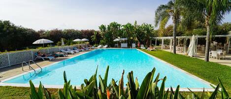 A rectangular swimming pool with a white deck, surrounded by palm trees and lounge chairs.