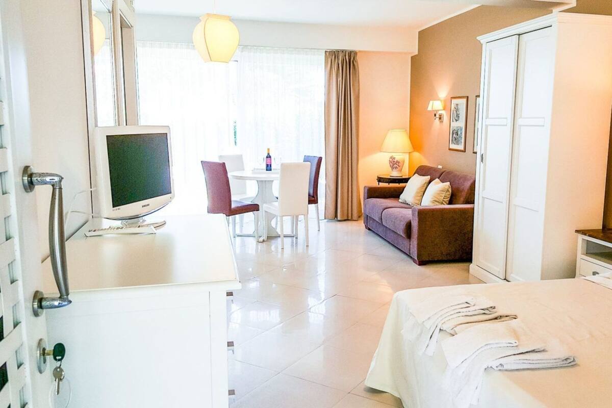 A hotel room with a bed, a desk with a computer, a sofa, and a dining table with chairs.