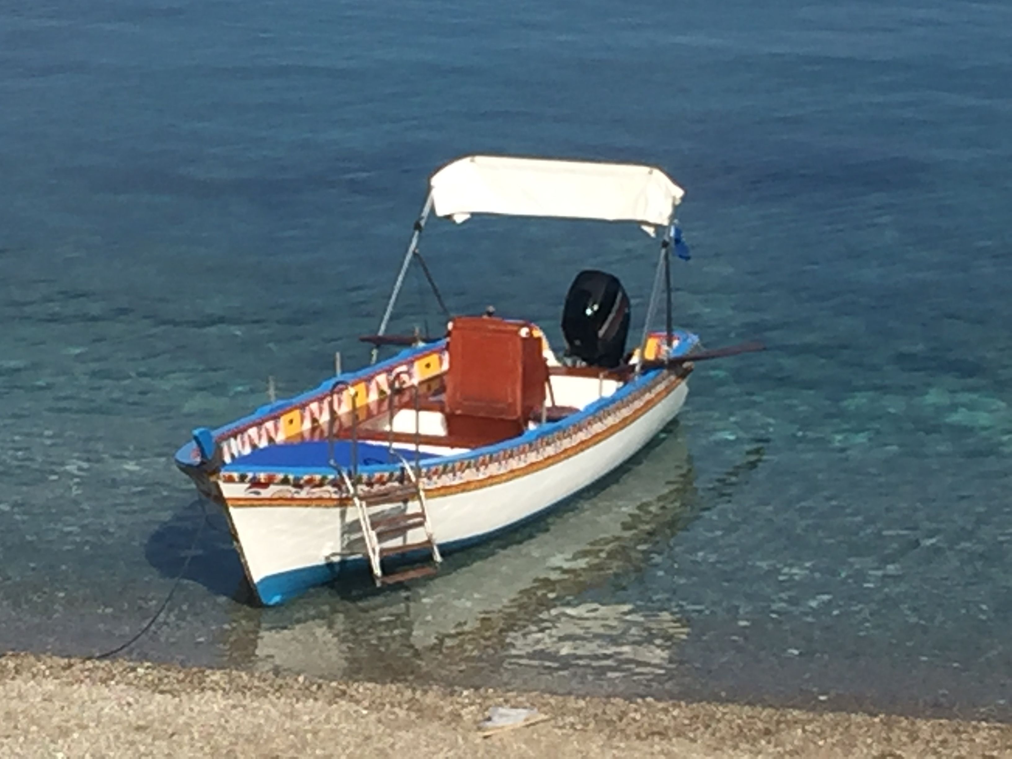 Ein kleines Boot mit weißem Verdeck, Motor und hölzernem Sitz, das auf klarem Wasser schwimmt.