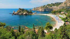 A coastal area with a beach, clear water, rocky outcrops, and a row of beach umbrellas. - Villa Oasis Residence (Taormina)