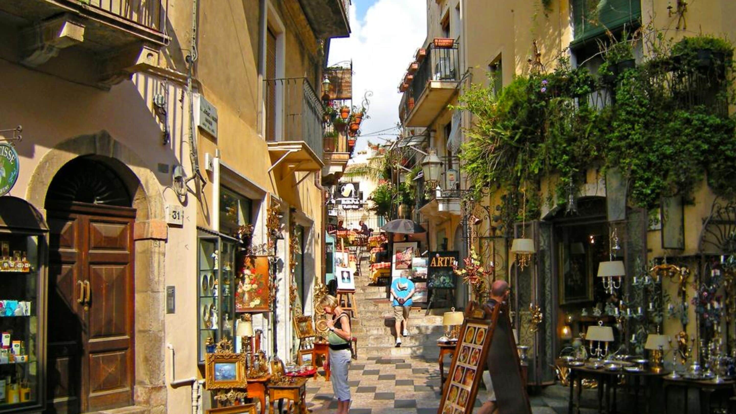 A narrow street with shops on both sides, featuring various items for sale.