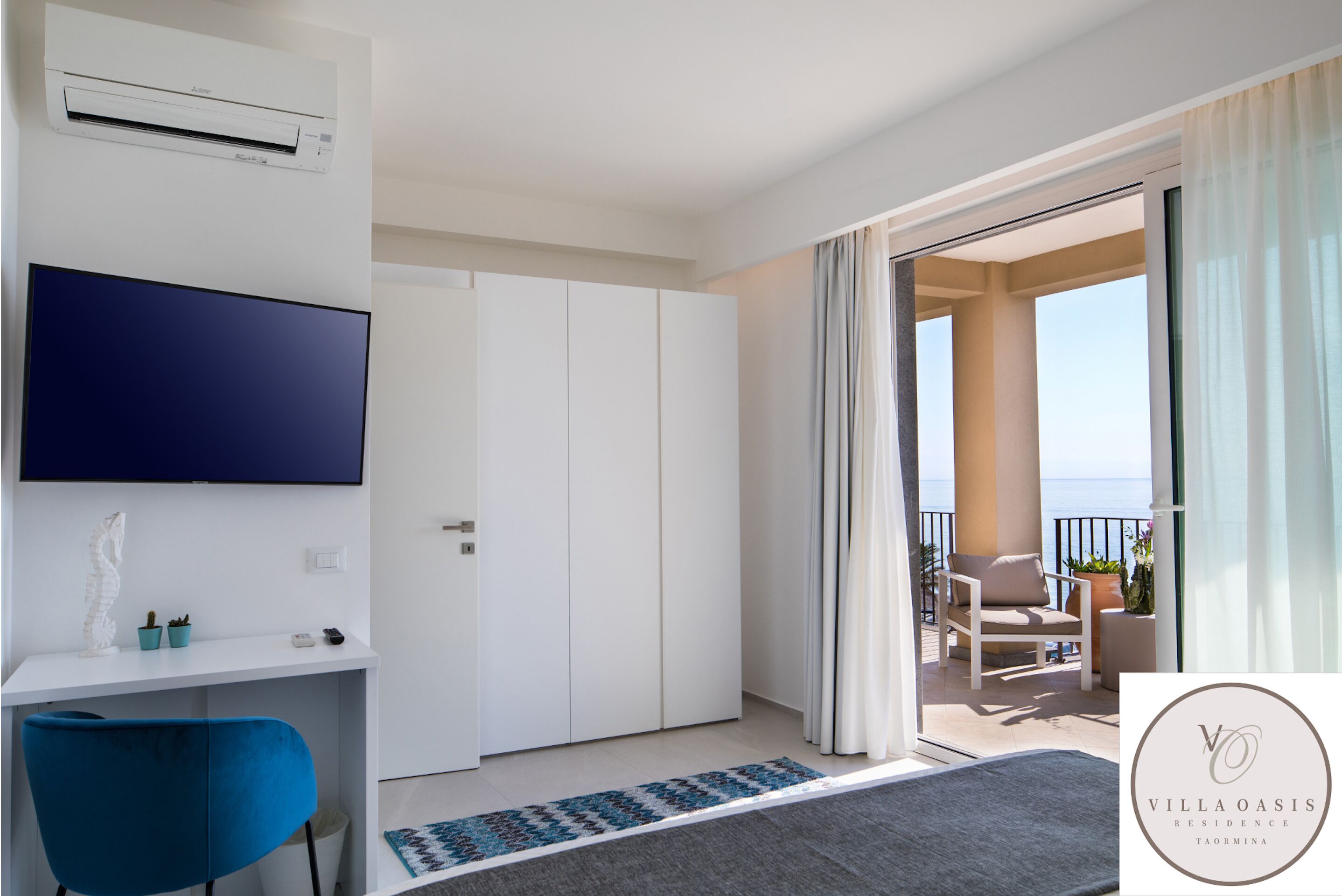 Ein modernes Hotelzimmer mit Flachbildfernseher, Schreibtisch mit Stuhl, Kleiderschrank und Balkon mit Meerblick.