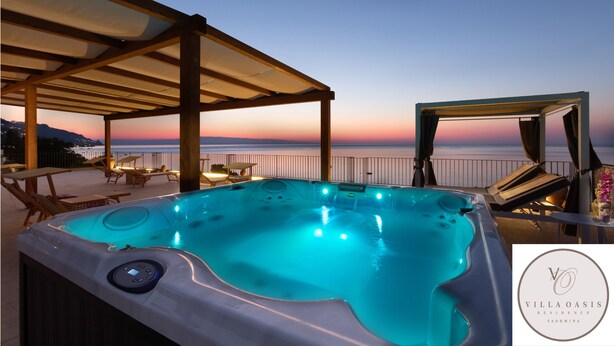 A hot tub with a control panel, surrounded by lounge chairs and tables, overlooking a sunset view. - Villa Oasis Residence (Taormina)