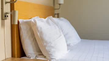 Een hotelkamer met een houten hoofdeinde, witte beddengoed en een afstandsbediening op een nachtkastje van hout.