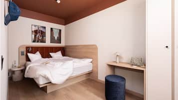 Una camera da letto con un letto, un comodino, una lampada e uno sgabello rotondo.