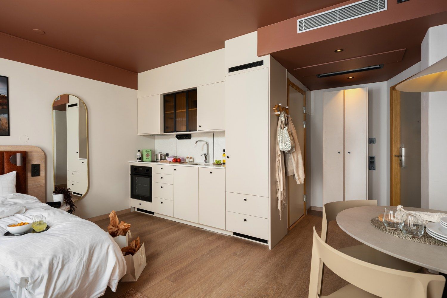 A compact hotel room with a bed, a small kitchenette, a dining area, and a bathroom.