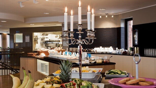A buffet area with various food items, a candelabra, and a kitchen in the background. - Sky Hotel Malmö City (Malmö)