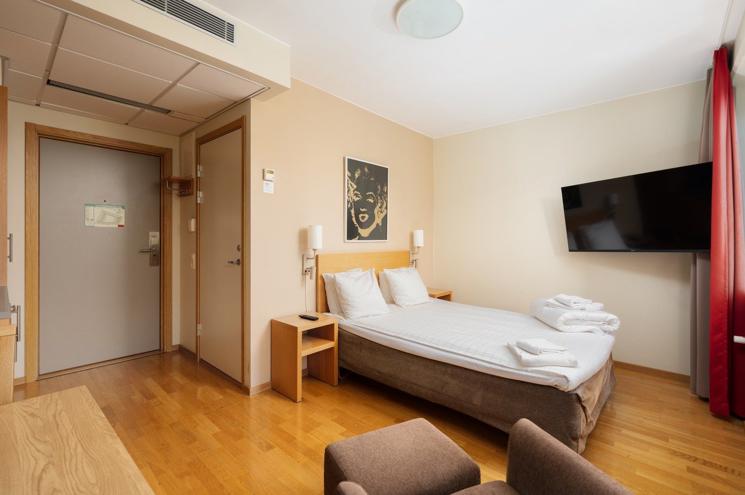 Ein Hotelzimmer mit Bett, Nachttisch, Fernseher und einem Gemälde an der Wand.