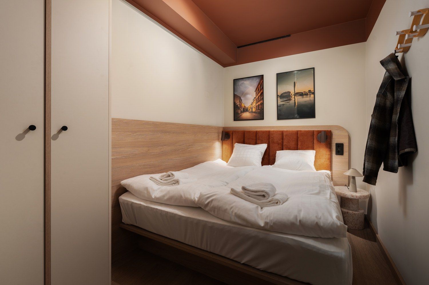 Habitación de hotel con una cama, una mesita de noche, una lámpara y dos cuadros en la pared.