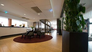 A lobby with a reception desk, seating area, staircase, and a large planter with greenery. - Sky Hotel Malmö City (Malmö)