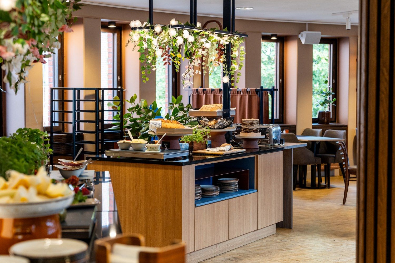 Una habitación de hotel moderna con una encimera central tipo isla, un comedor con sillas y ventanas grandes que permiten la entrada de luz natural.