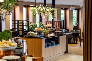 Una habitación de hotel moderna con una encimera central tipo isla, un comedor con sillas y ventanas grandes que permiten la entrada de luz natural.