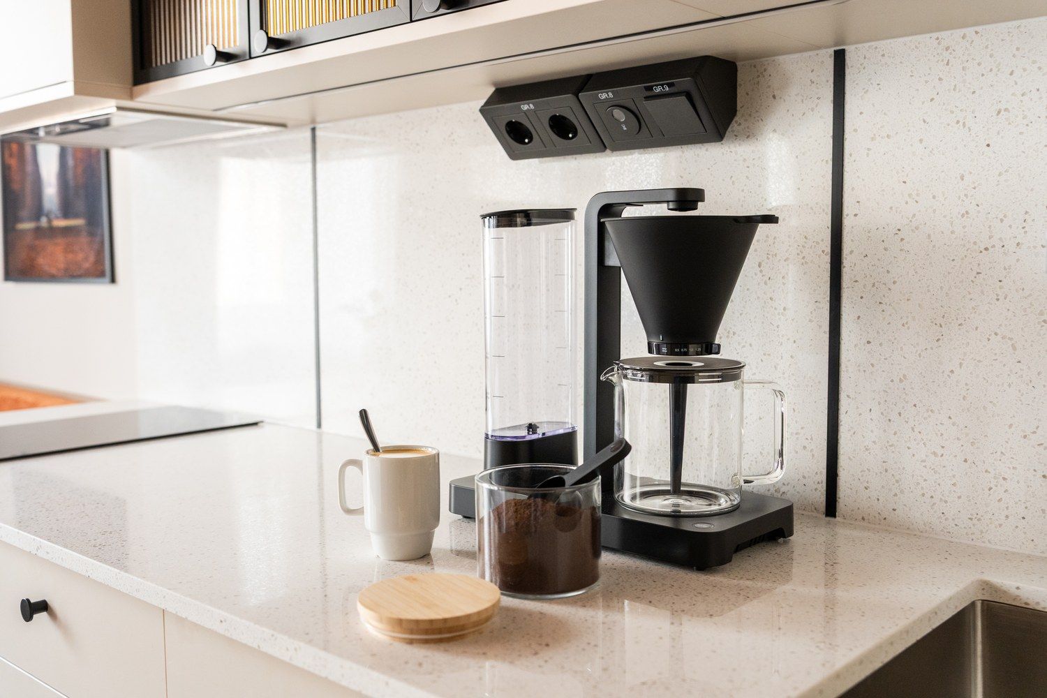 Ett modernt kök med en kaffebryggare, en mugg och en glaskaraff på bänkskivan.