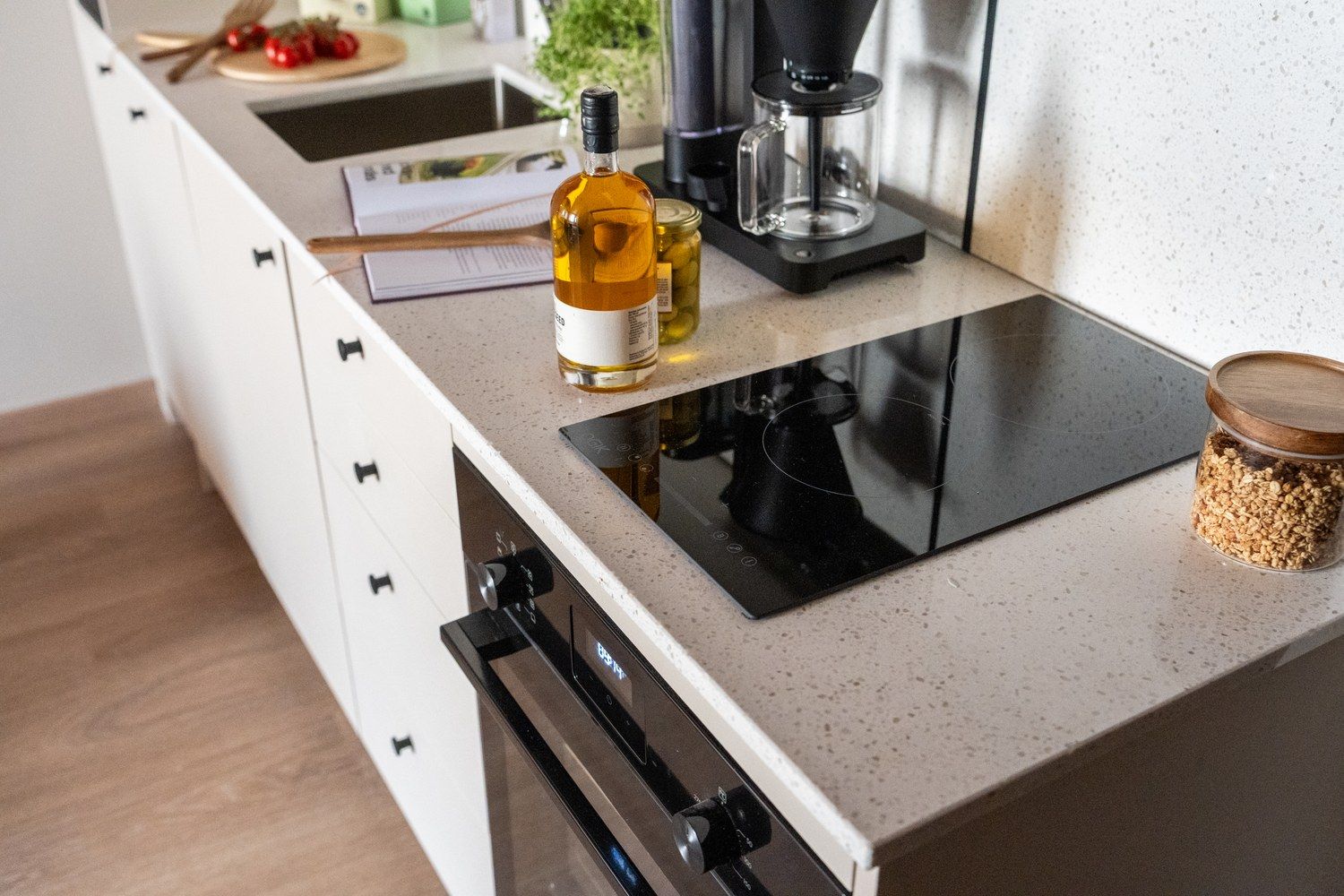 A kitchen with a built-in induction cooktop, a coffee maker, a bottle of olive oil, and a jar of oats.