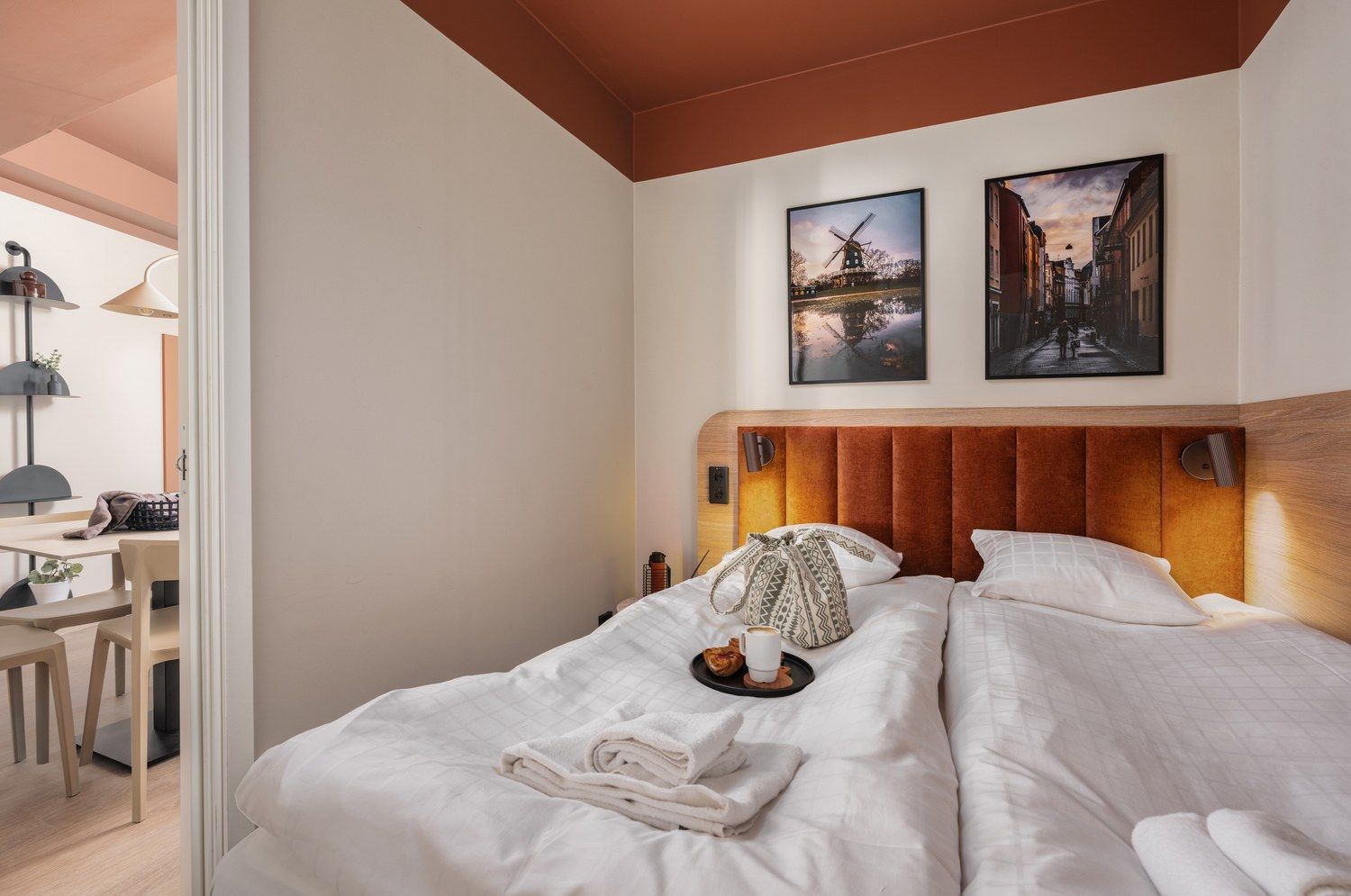 A hotel room with a bed, a desk, and two paintings on the wall.