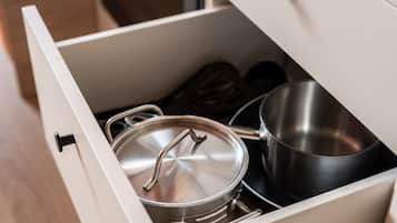 A drawer containing a stainless steel pot with a lid, a black saucepan, and a pair of wooden spoons.
