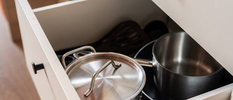 Un tiroir contenant une casserole en acier inoxydable avec un couvercle, une petite casserole noire et une paire de cuillères en bois.