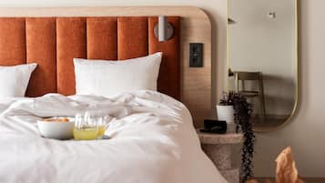 A neatly made bed with white bedding, a bedside table with a bowl of cereal and a glass of juice, and a mirror with a gold frame.
