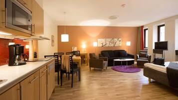 A modern hotel room with a kitchenette, dining area, and seating space.
