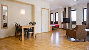 A modern hotel room with a wooden dining table, chairs, a bed with a red blanket, a TV, and large windows. - Sky Hotel Malmö City (Malmö)