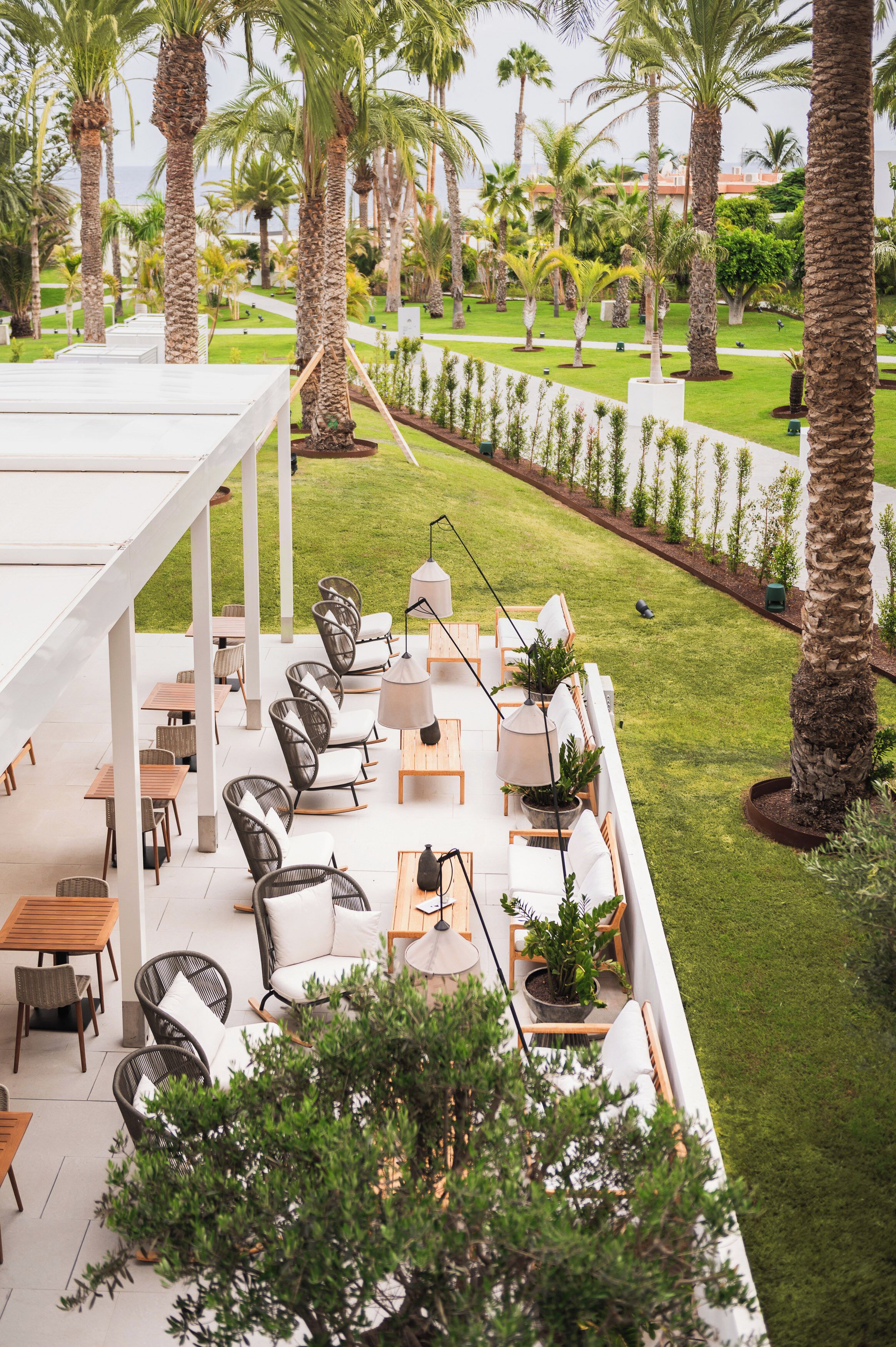An outdoor patio area with seating and tables, surrounded by palm trees and a well-maintained lawn.