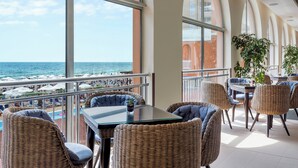 A balcony with wicker furniture, a glass table, and a view of the beach and ocean. - Sol Luna Bay Resort (Byala)