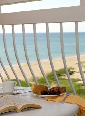 A table with a book, a cup, a plate with croissants and cherries, and a fork, overlooking a beach. - Sol Luna Bay Resort (Byala)