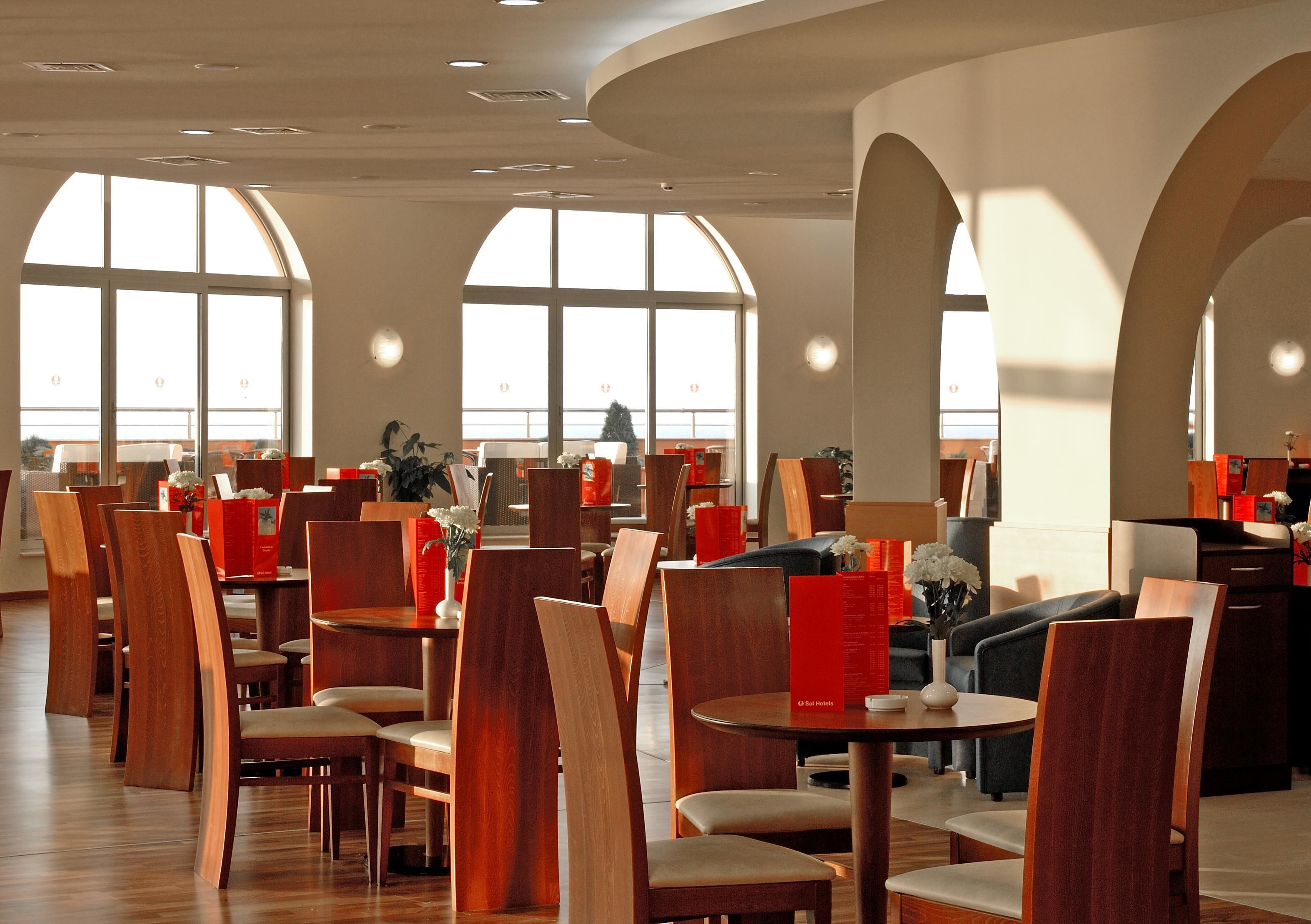A spacious restaurant with high wooden chairs and tables, large windows, and a modern interior design.