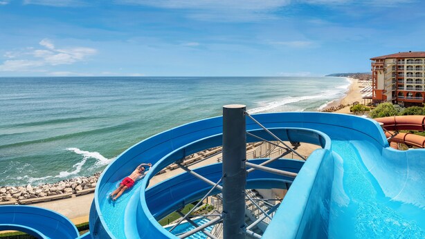 A water slide at a beachside resort with a view of the ocean and a hotel in the background. - Sol Luna Bay Resort (Byala)