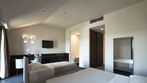 A modern hotel room with a large bed, a desk, a chair, a TV, and a bathroom visible through an open door.