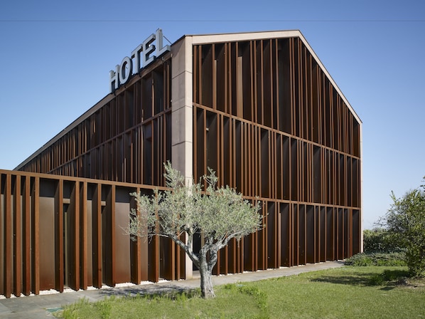 Un hotel moderno con un llamativo letrero que dice 'HOTEL', que presenta un diseño arquitectónico único con paneles verticales de madera y un patio central con un árbol.