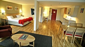 Ein Hotelzimmer mit Bett, Schreibtisch, Stuhl, Tisch und einer Küchenzeile.