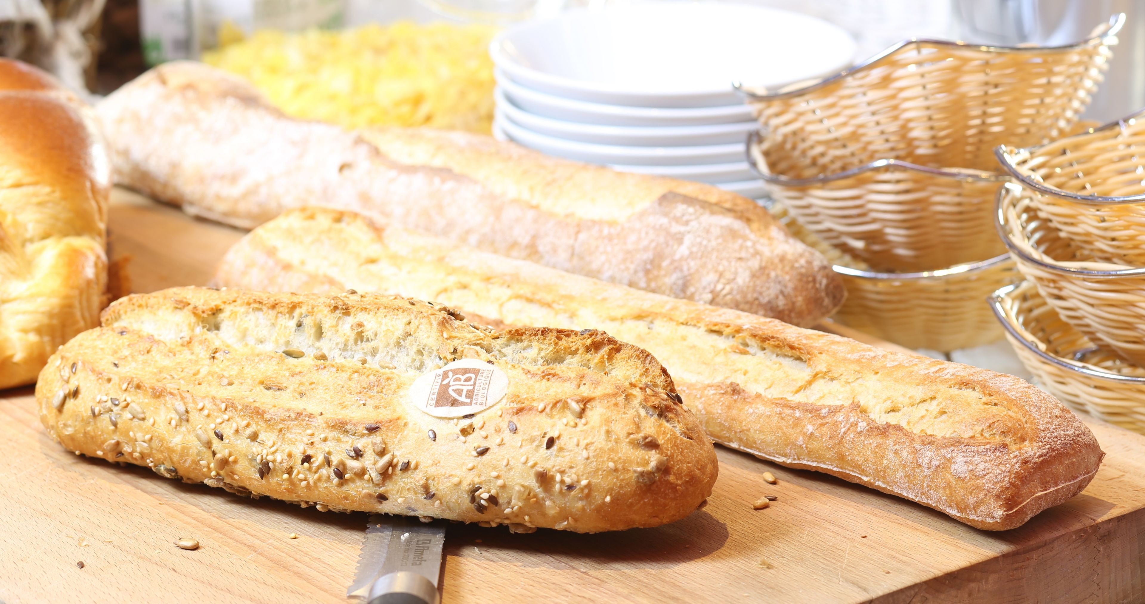 A variety of breads on a wooden surface, including a baguette and a loaf with seeds.