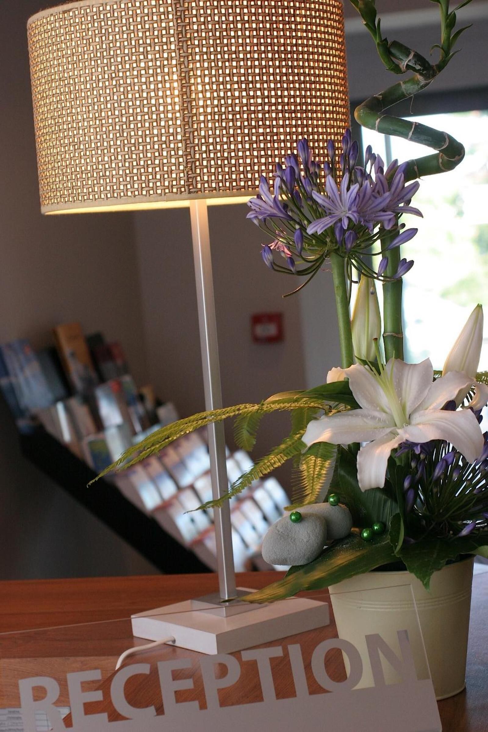 Un mostrador de recepción con una lámpara, una planta en maceta con flores y un cartel que dice 'RECEPTION'.