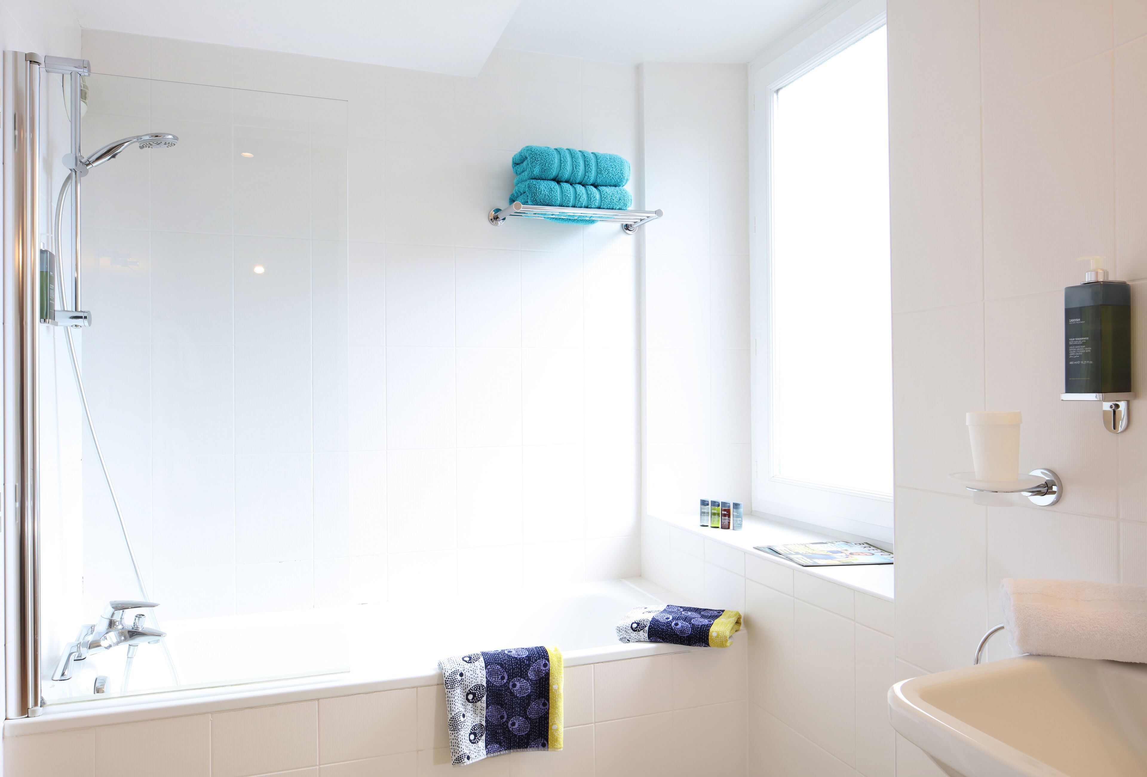 A modern bathroom with a glass-enclosed shower, a bathtub, and a window providing natural light.