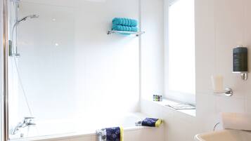 A modern bathroom with a glass-enclosed shower, a bathtub, and a window providing natural light.
