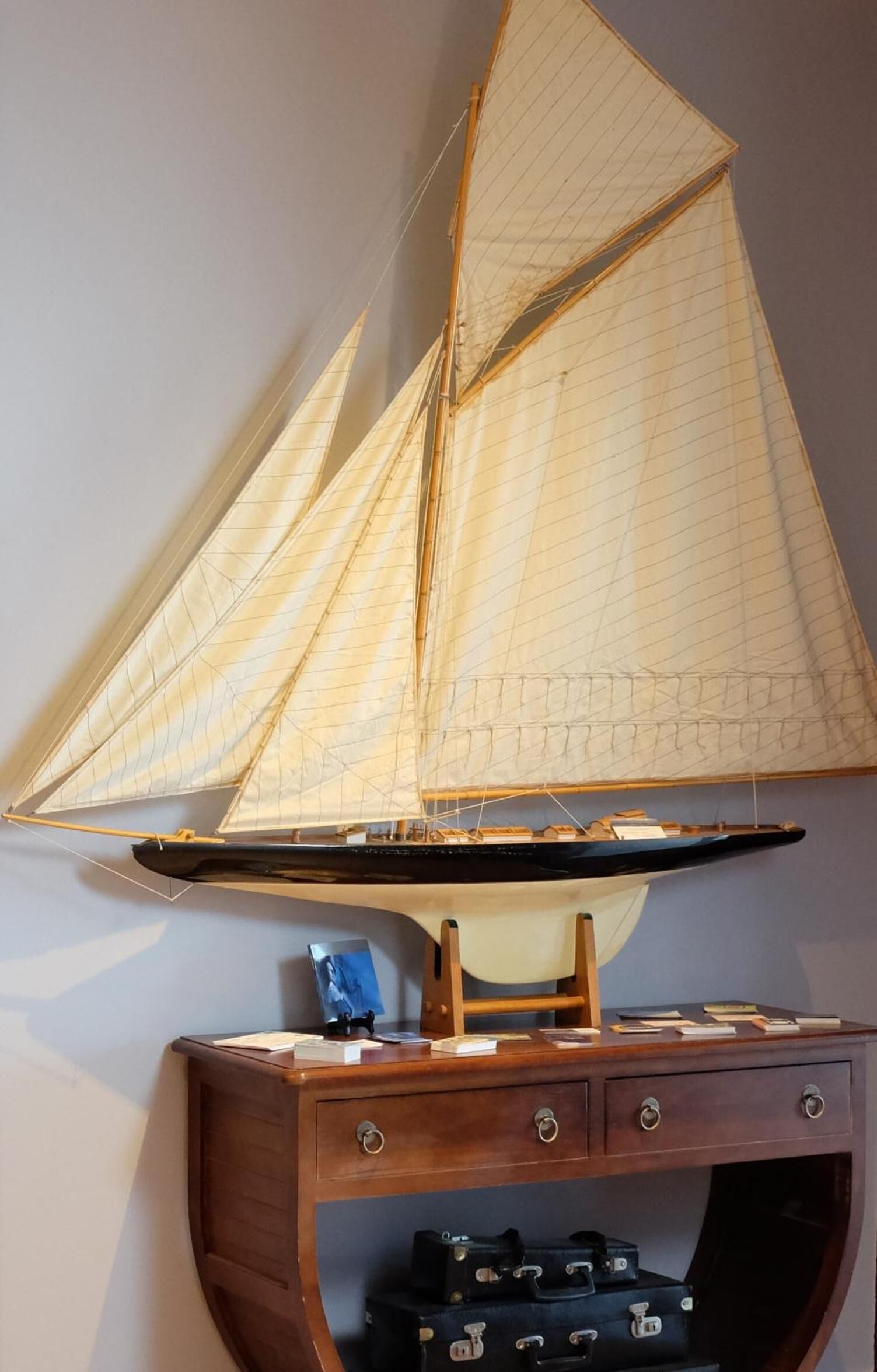 Ein Modellsegelboot auf einem hölzernen Ständer, darunter Schubladen.