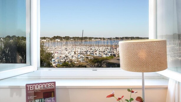 Habitación de hotel con vistas a un puerto deportivo, un escritorio con teléfono, una revista y una planta en maceta.